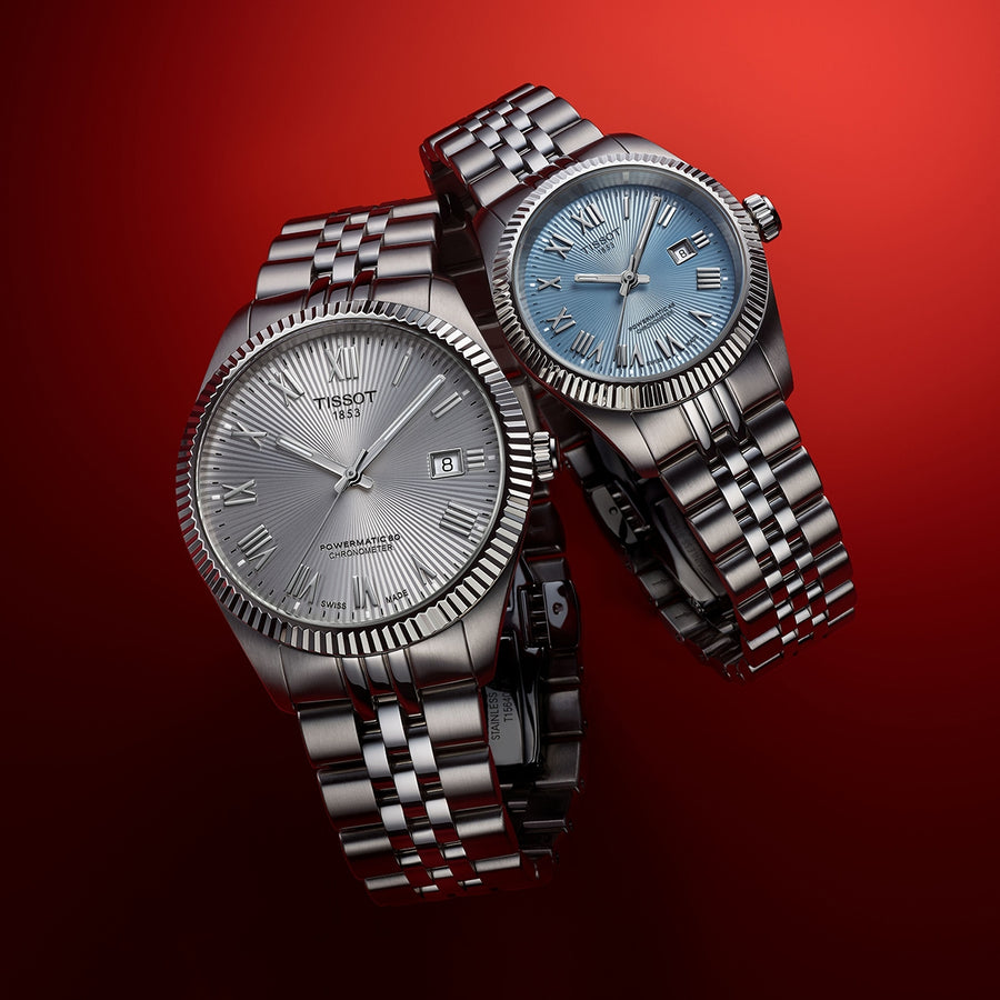 Deux montres Tissot en acier, cadrans argenté et bleu glacier, lunettes cannelées, chiffres romains, sur fond rouge